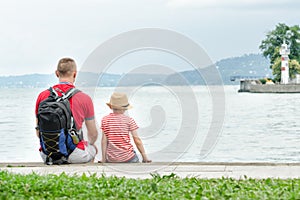 Father and son sitting on the pier. Sea, lighthouse and mountain