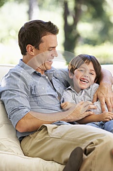 Father And Son Sitting On Sofa At Home