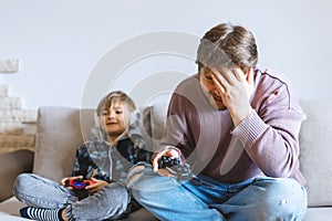 Father And Son Sitting On Sofa In Lounge Playing Video Game