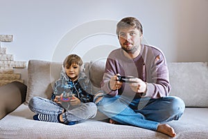 Father And Son Sitting On Sofa In Lounge Playing Video Game