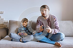 Father And Son Sitting On Sofa In Lounge Playing Video Game