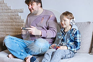 Father And Son Sitting On Sofa In Lounge Playing Video Game