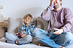 Father And Son Sitting On Sofa In Lounge Playing Video Game