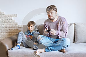 Father And Son Sitting On Sofa In Lounge Playing Video Game