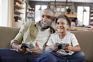 Father And Son Sitting On Sofa In Lounge Playing Video Game