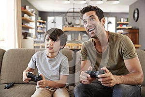 Father And Son Sitting On Sofa In Lounge Playing Video Game