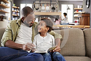 Father And Son Sitting On Sofa In Lounge Reading Book Together