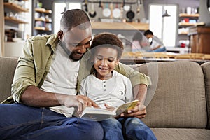 Father And Son Sitting On Sofa In Lounge Reading Book Together