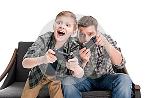 Father and son sitting on sofa and playing with joysticks
