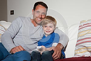 Father And Son Sitting On Sofa Watching TV Together