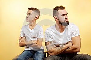 Father and son sitting together against yellow background. Quarrel, resentment, insult, offense concept