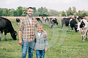 father and son smiling at camera while standing near grazing cattle
