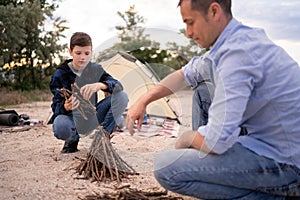 Father and son spending happy leisure time together outdoors in the camp. Family man child making campfire on nature