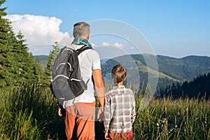 Father with son are standing on a alpine meadow among a lush grass