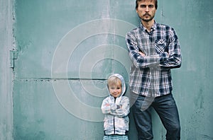 Father and son standing near blue wall with they arms crossed over chest and looking to camera. Fathers day, parenting, two