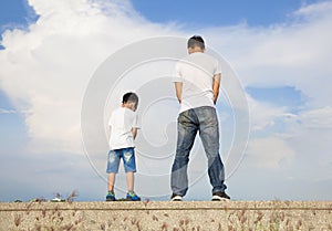 Father and son standing on a stone platform and pee together