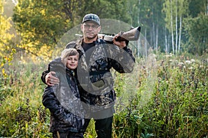 Father and son standing together outdoors with shotgun hunting gear.