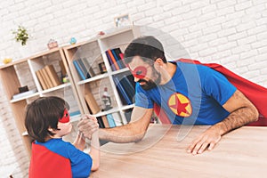 Father and son in suits of superheroes. They compete in arm wrestling. They are measure their strength