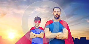 Father and son in superhero capes over city