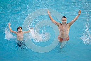 Father and son swimming in pool, summer family weekeng. Little kid boy with father splashing in swimming pool. Family