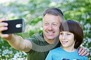 Father and son taking photo with smartphone together outdoor. Family selfie time