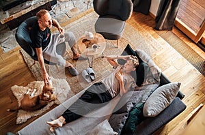 Father and son together at the home living room. Boy lying in comfortable sofa and his daddy stroking their beagle dog and smiling