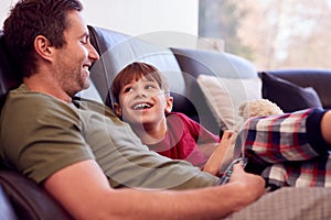 Father And Son With Toy Dog Sitting On Sofa In Pyjamas Together Watching TV