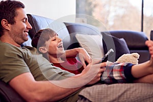 Father And Son With Toy Dog Sitting On Sofa In Pyjamas Together Watching TV