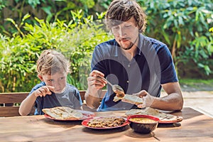 Father and son try Indian food in a cafe on the street