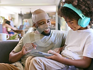 Father And Son Using Digital Tablet With Headphones At Home With Multi-Generation Family Behind