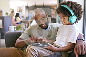 Father And Son Using Digital Tablet With Headphones At Home With Multi-Generation Family Behind
