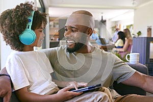 Father And Son Using Digital Tablet With Headphones At Home With Multi-Generation Family Behind