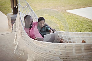 Father and son using laptop while relaxing on hammock