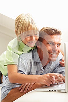 Father And Son Using Laptop Sitting On Sofa