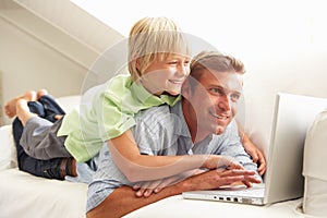 Father And Son Using Laptop Sitting On Sofa