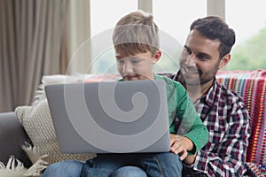 Father and son using laptop on sofa in a comfortable home