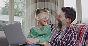 Father and son using laptop on sofa in a comfortable home 4k
