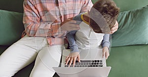 Father and son using laptop on sofa at home 4k