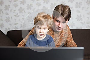 Father and son using laptop together on sofa at home