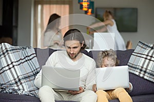 Father and son using laptops sitting on sofa at home