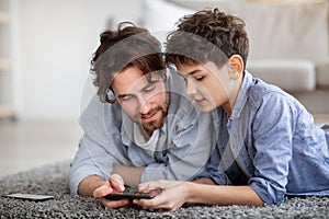 Father and son using smartphone, watching photos or boy helping daddy with game, spending time at home