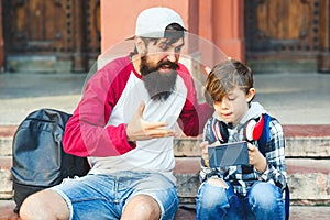 Father and son are using smartphones. Young dad and son enjoy leisure time spent together. Leisure, technology, family and people