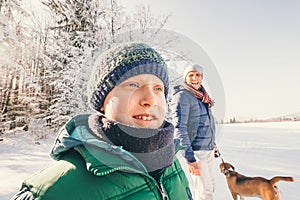 Father and son walk with dog in snow forest at sunny winter day