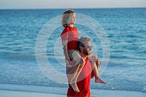 Father and son walk in sea beach. Concept of friendly family. Son on fathers shoulders piggyback ride. Dad with kid