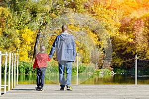 Father and son are walking along the pier. Autumn, sunny. Back v