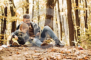 Father and son walking in autumn forest at sunset. Sweetheart child and bearded dad lie on fall autumnal yellow leaves