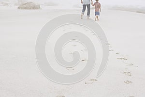 Father And Son Walking Leaving Behind Footprints On Sand