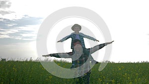 Father and son walking on meadow, child sits on shoulders dad and play airplane with arms raised on rapeseed field on