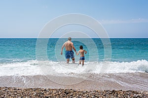 Father and son walking into the sea in Greece