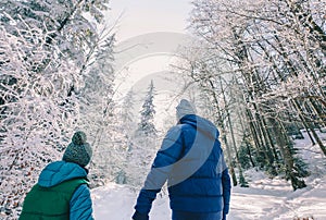 Father and son walking in a snowy forest. They enjoying the branches covered with snow. Dad and son relatives concept image